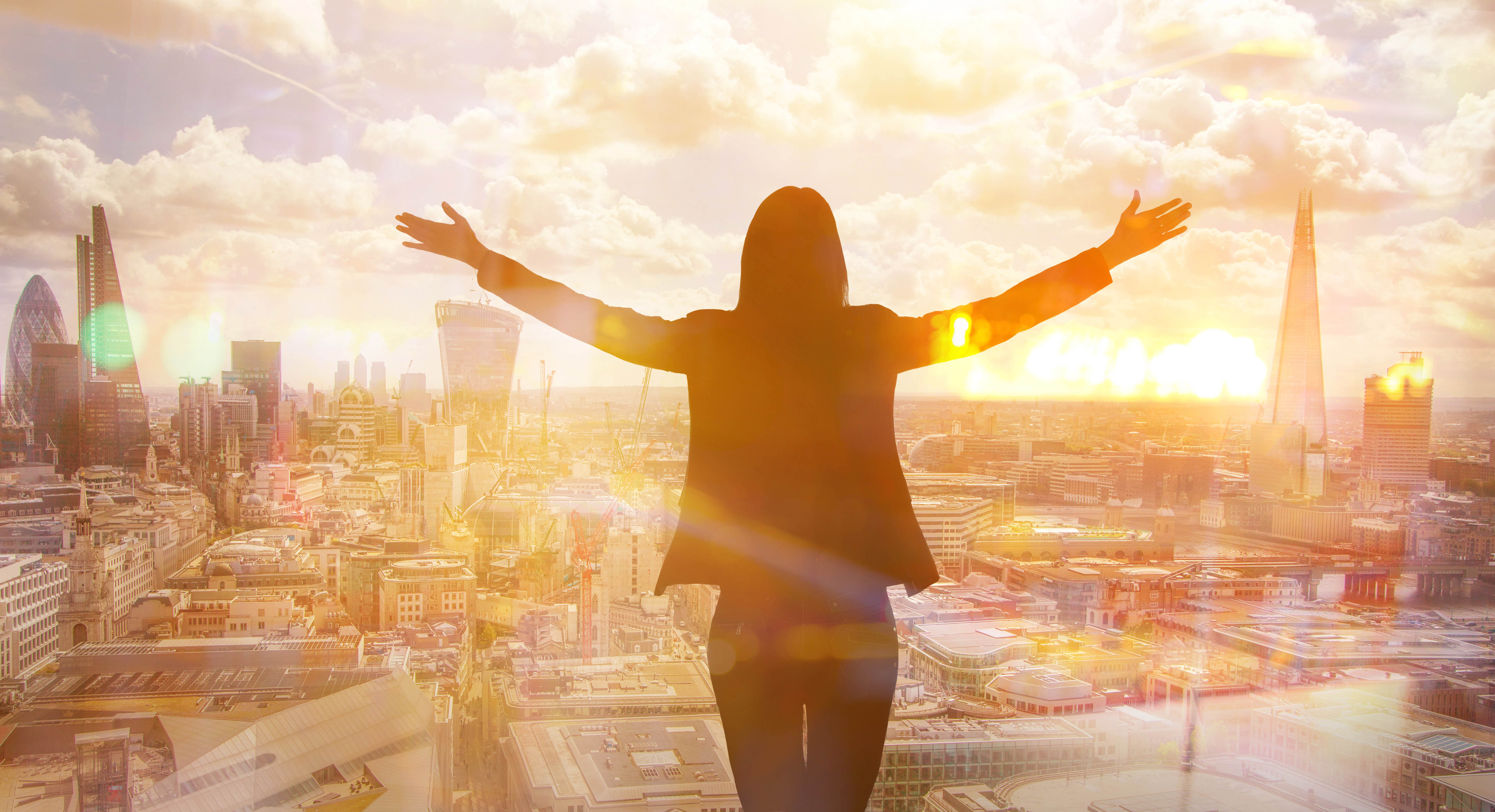 Woman standing with her arms raised, staring out at a city Woman standing with her arms raised, staring out at a city